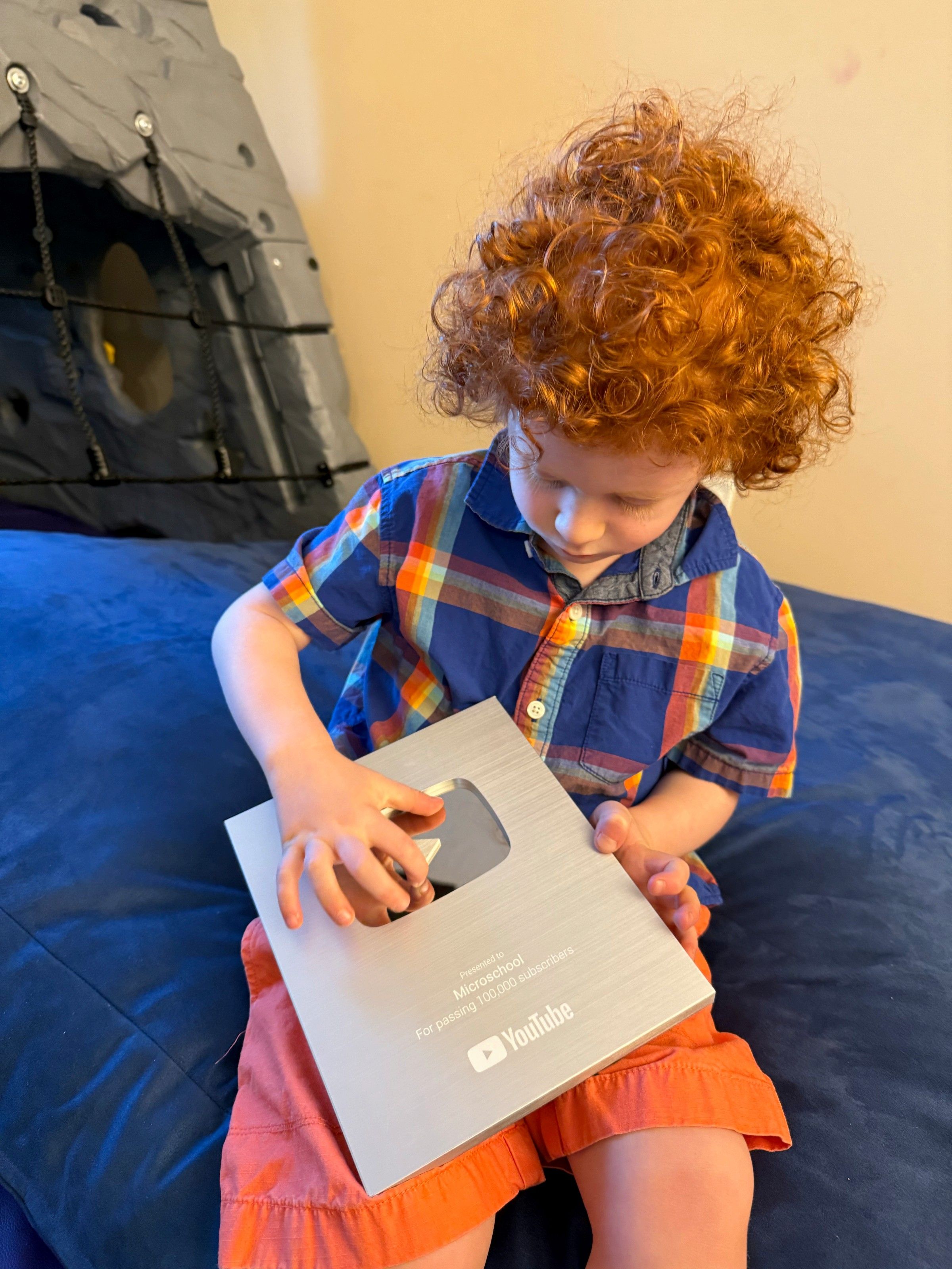 Child sitting outdoors holding the YouTube Silver Play Button award